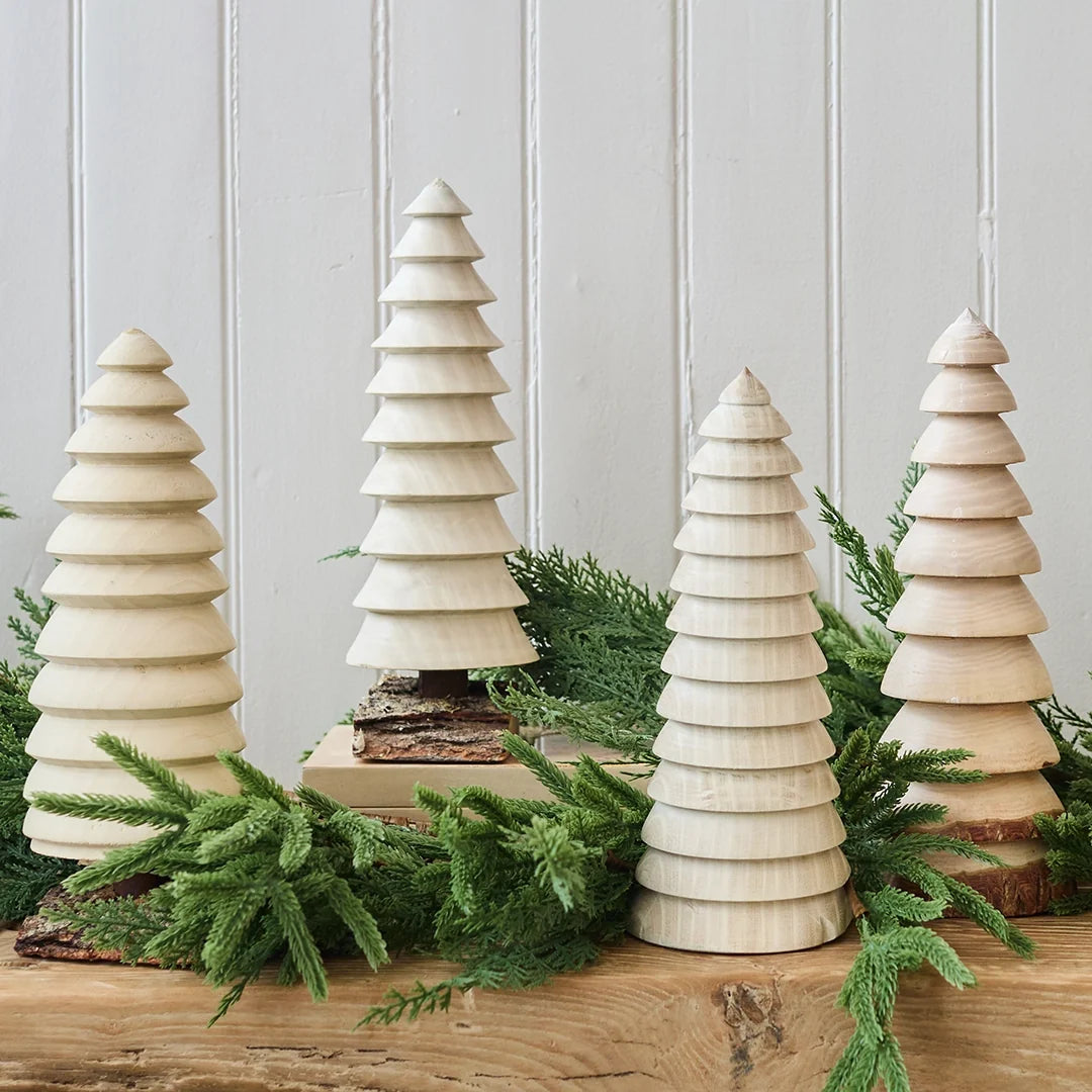 Set of wooden Christmas trees with greenery on a wooden surface against a light gray wall.