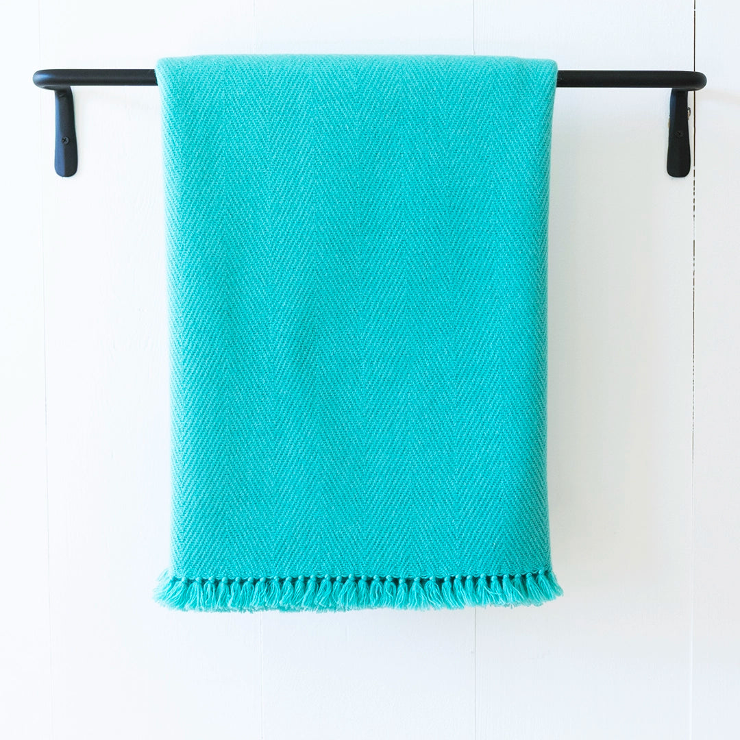 Nantucket Looms handwoven cashmere throw blanket in Glacier Blue turquoise, draped over a black metal rack on a white background.