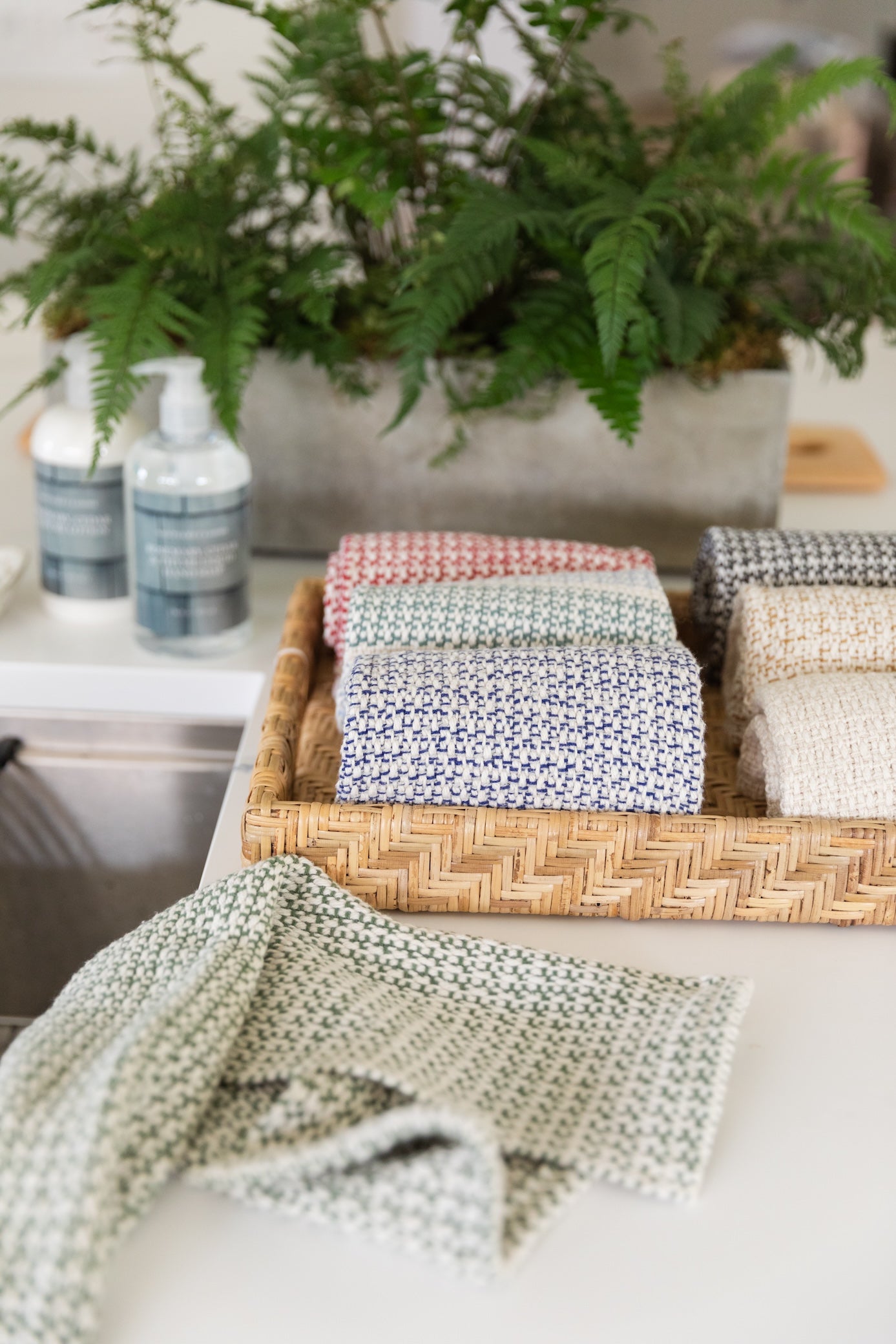 Collection of handwoven kitchen towels in various colors displayed in woven basket with ferns