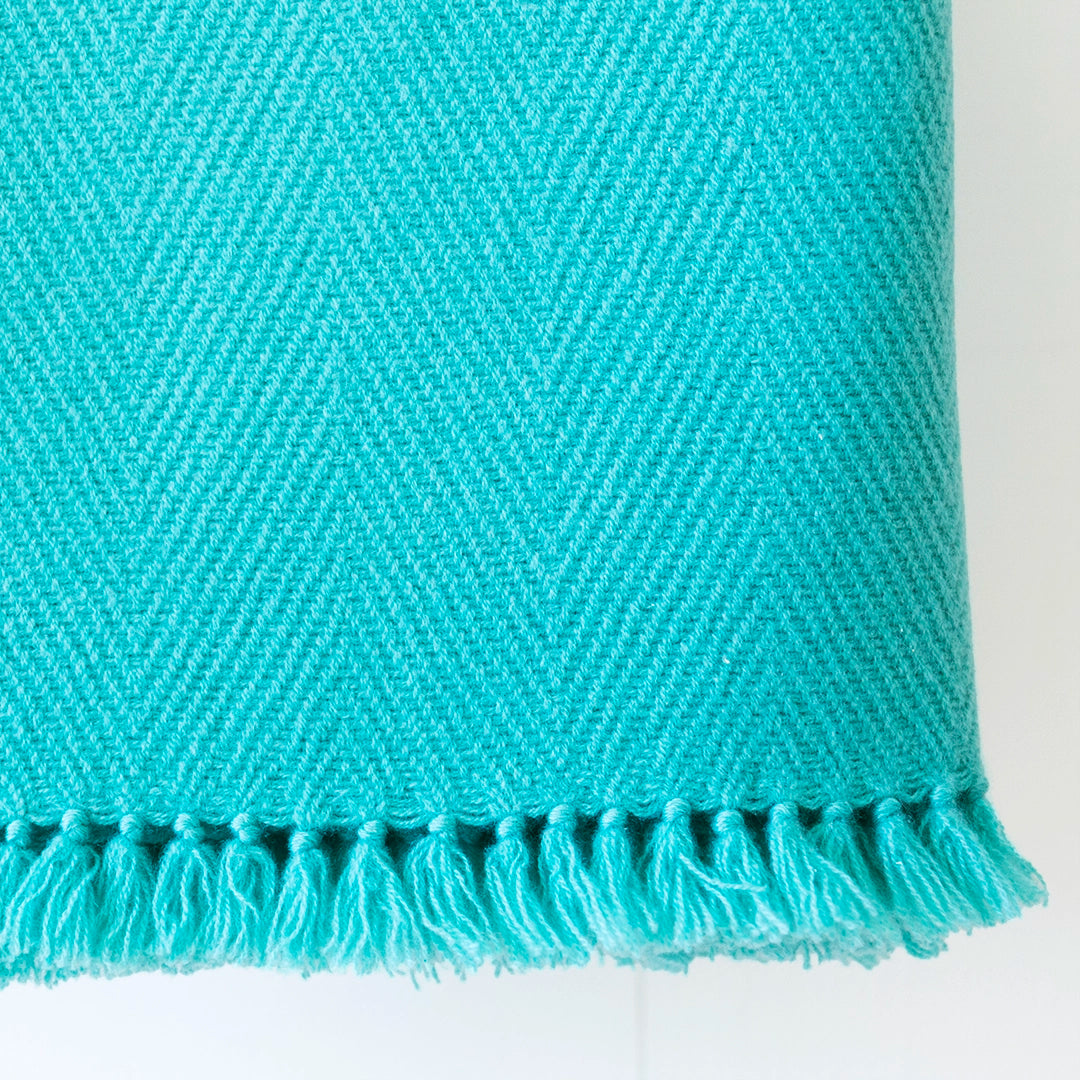Close-up of a Nantucket Looms handwoven cashmere throw blanket in Glacier Blue turquoise, showing the textured weave and tassels on a white background.