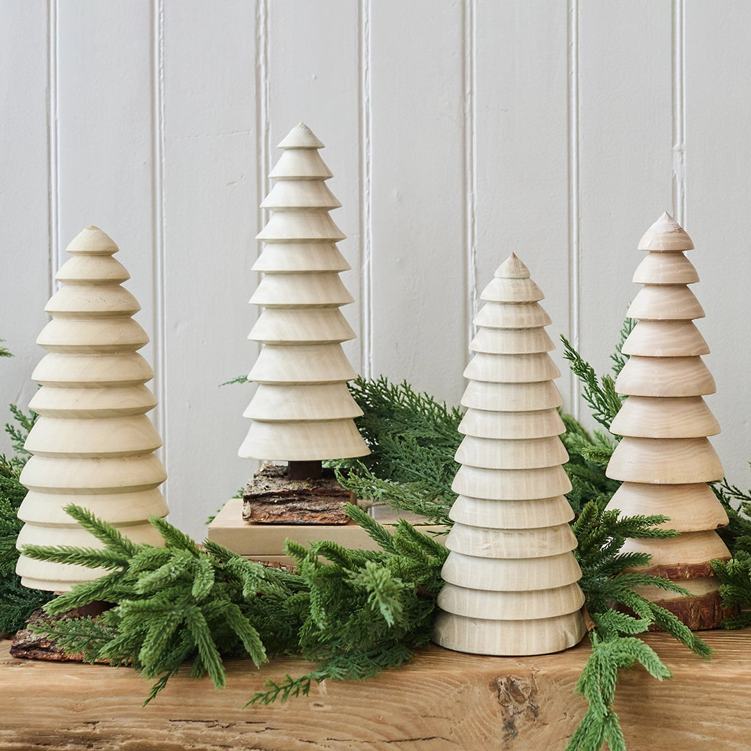 Set of wooden Christmas trees with greenery on a wooden surface against a light gray wall.