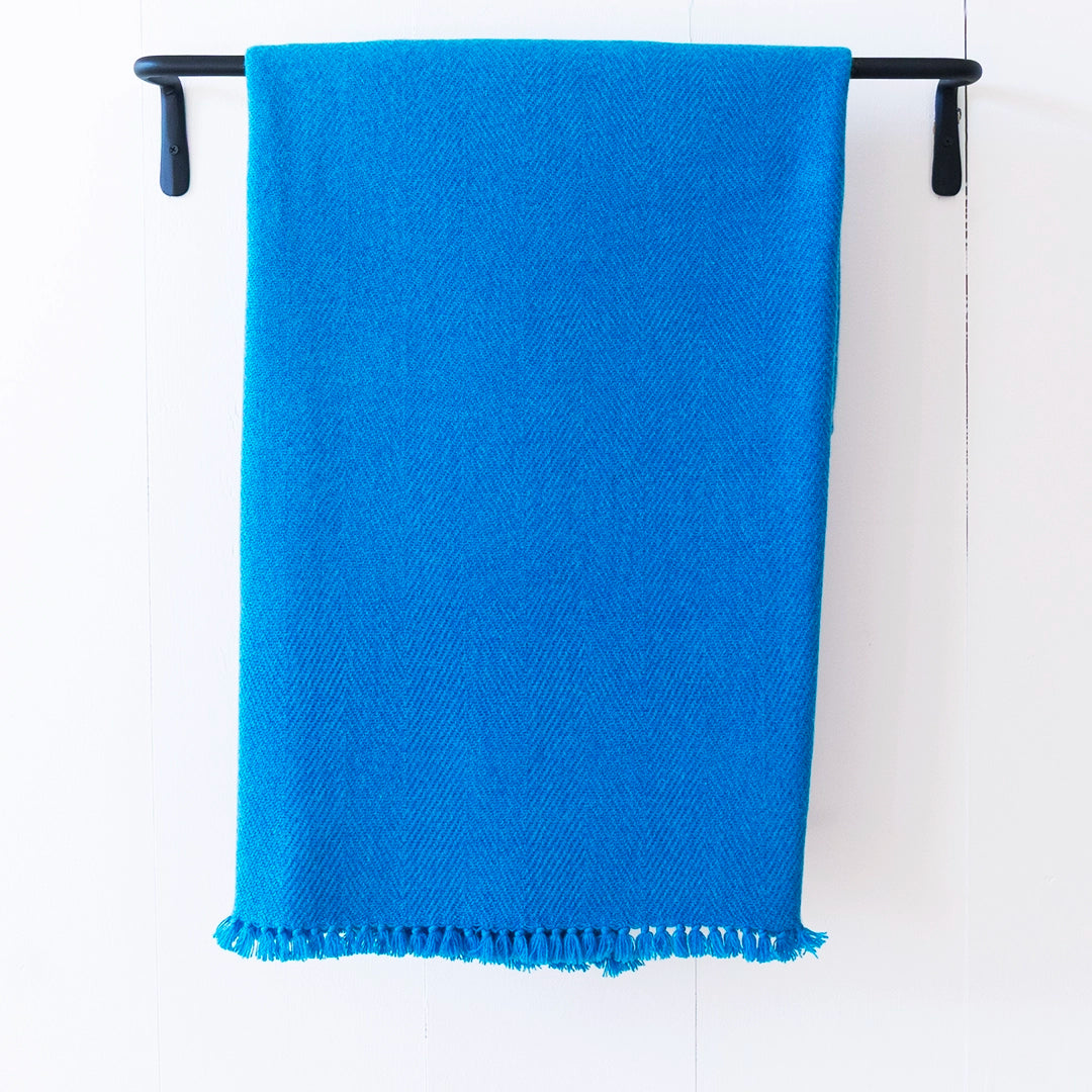 Nantucket Looms cashmere throw blanket in Hummingbird Blue, a soft muted blue, draped over a black metal rack on a white background.