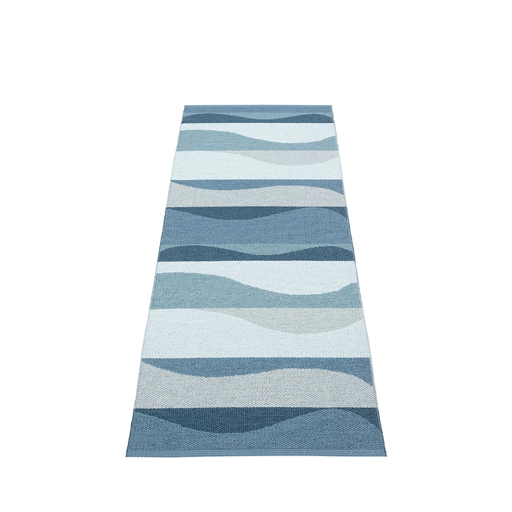 Textured Pappelina rug with a reversible design featuring flowing stripes in a cool blue palette, laid flat on an unadorned surface.